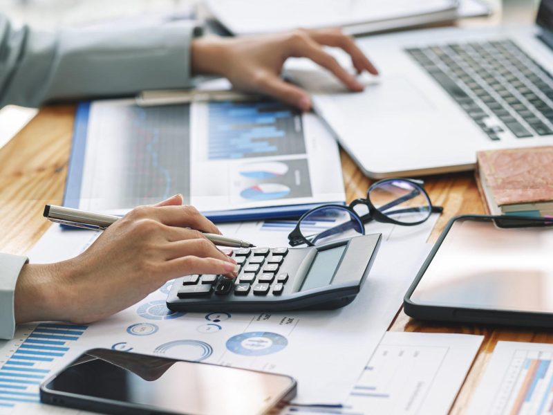 Businesswoman working at office with document on her desk, doing planning analyzing the financial report, business plan investment, finance analysis concept.Using calculator machine.